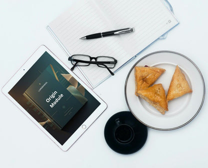 Tablet display Swift PDF course 'Origin Module' , glasses, plate with pastries, and coffee cup on a white surface